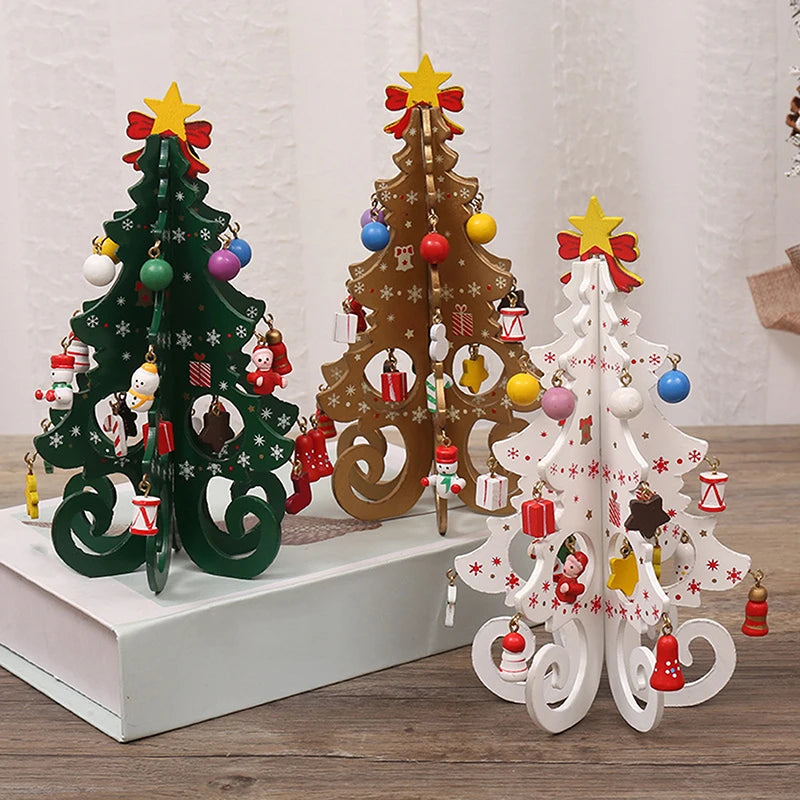 Três árvores de Natal decorativas feitas de madeira pintada, uma verde, uma marrom e uma branca, decoradas com enfeites natalinos rosa, vermelho, amarelo, branco e azul, incluindo presentes, estrelas, bonecos de neve e laços vermelhos, colocadas sobre uma mesa de madeira.