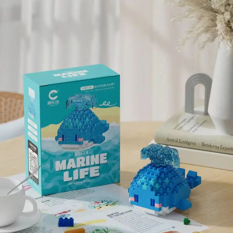 Peça de brinquedo em formato de baleia marinha feita com blocos de montar, com destaque para a cabeça azul translúcida, sobre uma mesa ao lado de uma caixa do produto "Marine Life".