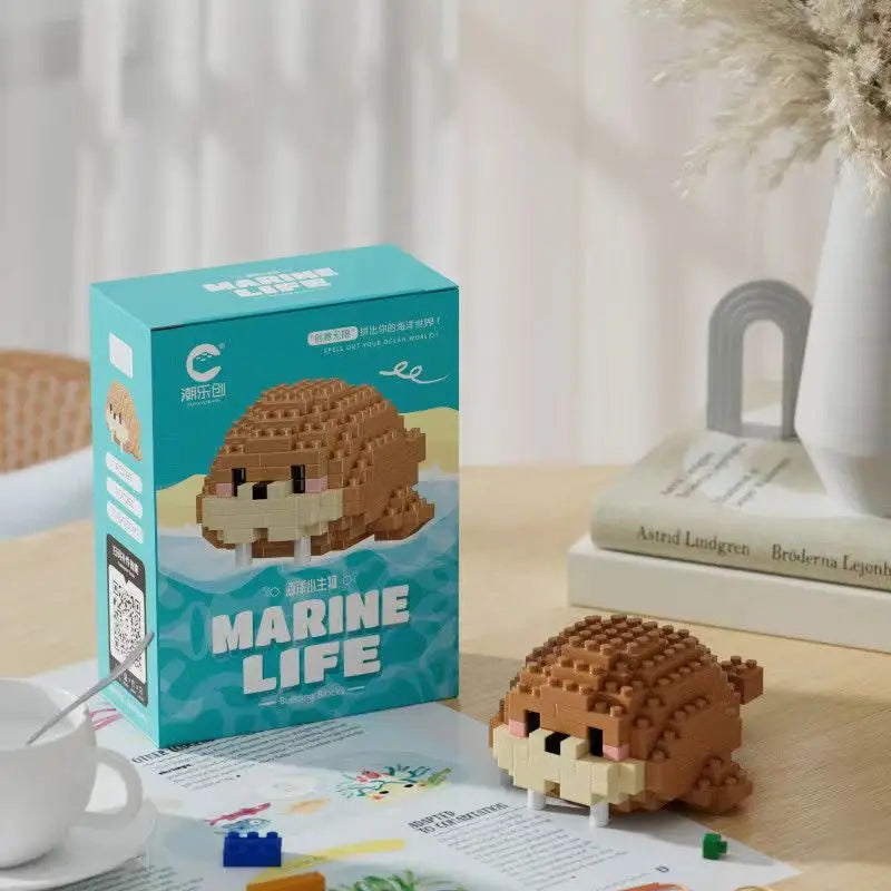 Pequeno brinquedo em formato de morsa em pixel art em tom de marrom com detalhes em preto e branco, acompanhado de uma caixa de embalagem chamada Marine Life.